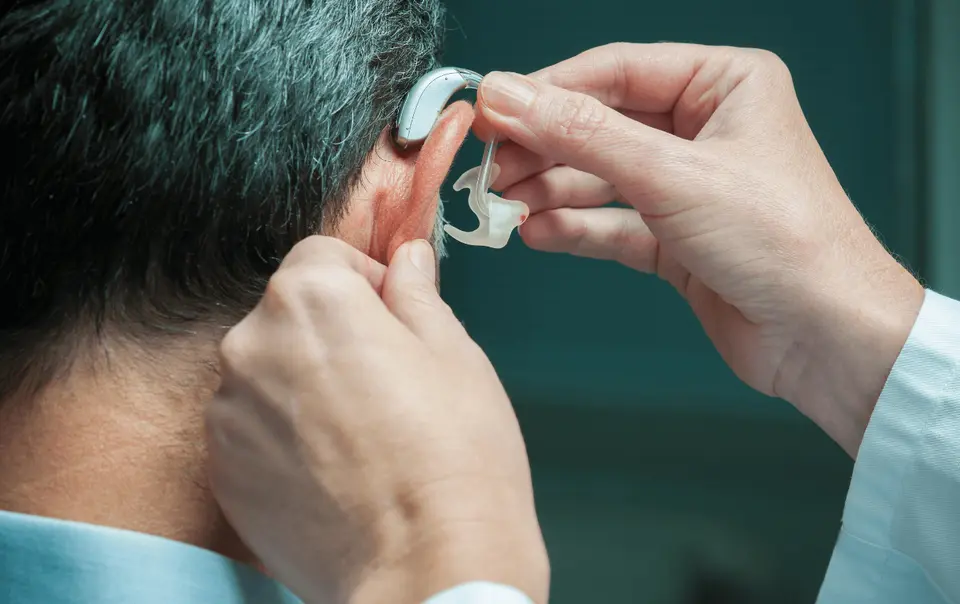 Audiologist fitting hearing aid on patient